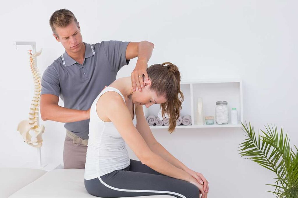 Chiropractic clinician discussing spinal treatment risks with an adult patient in a bright exam room.